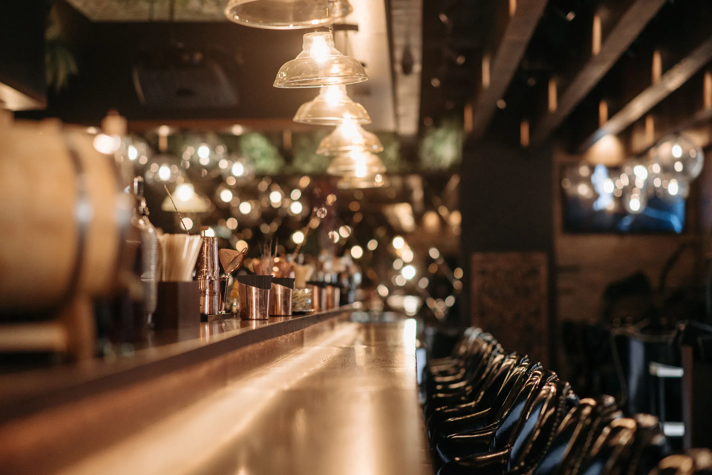 The long bar at night: copper, glass and a row of empty stools under low lights