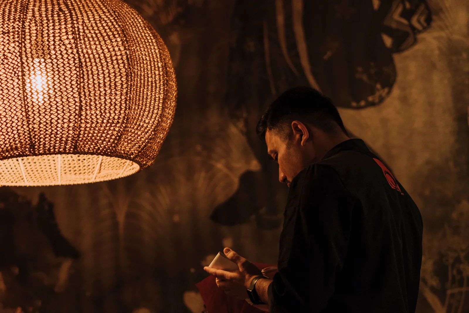 A bartender stirring a drink under a woven pendant lamp