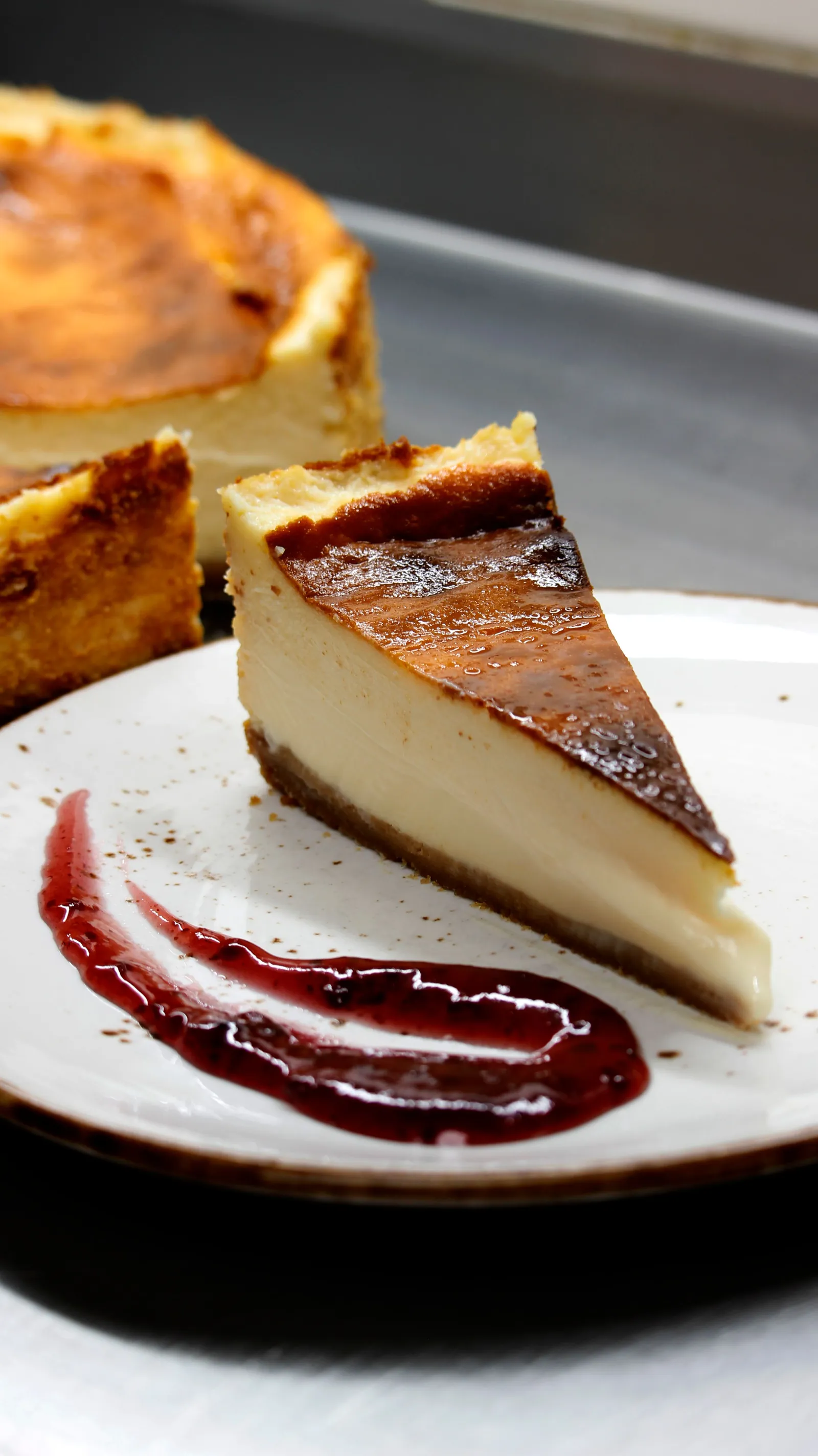 A slice of burnt cheesecake with a dark caramelised top and berry sauce