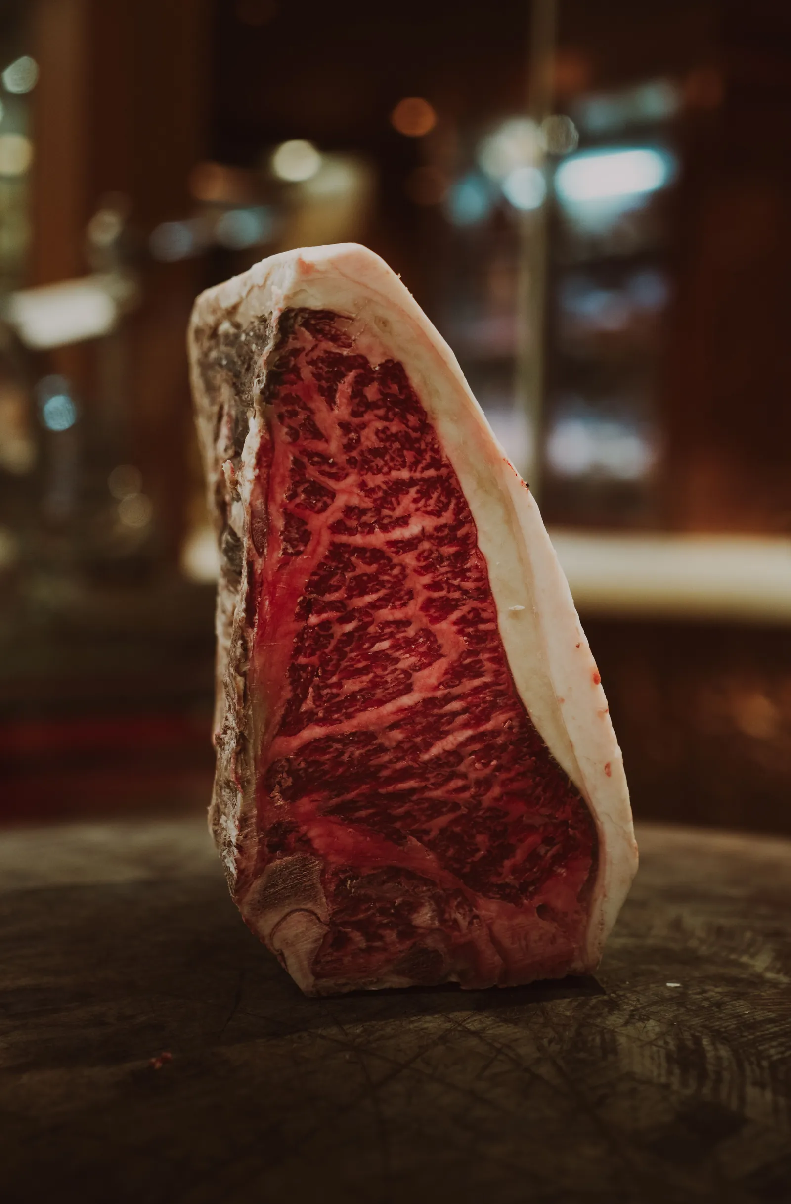 A thick dry-aged steak standing on its edge in a dark cold room