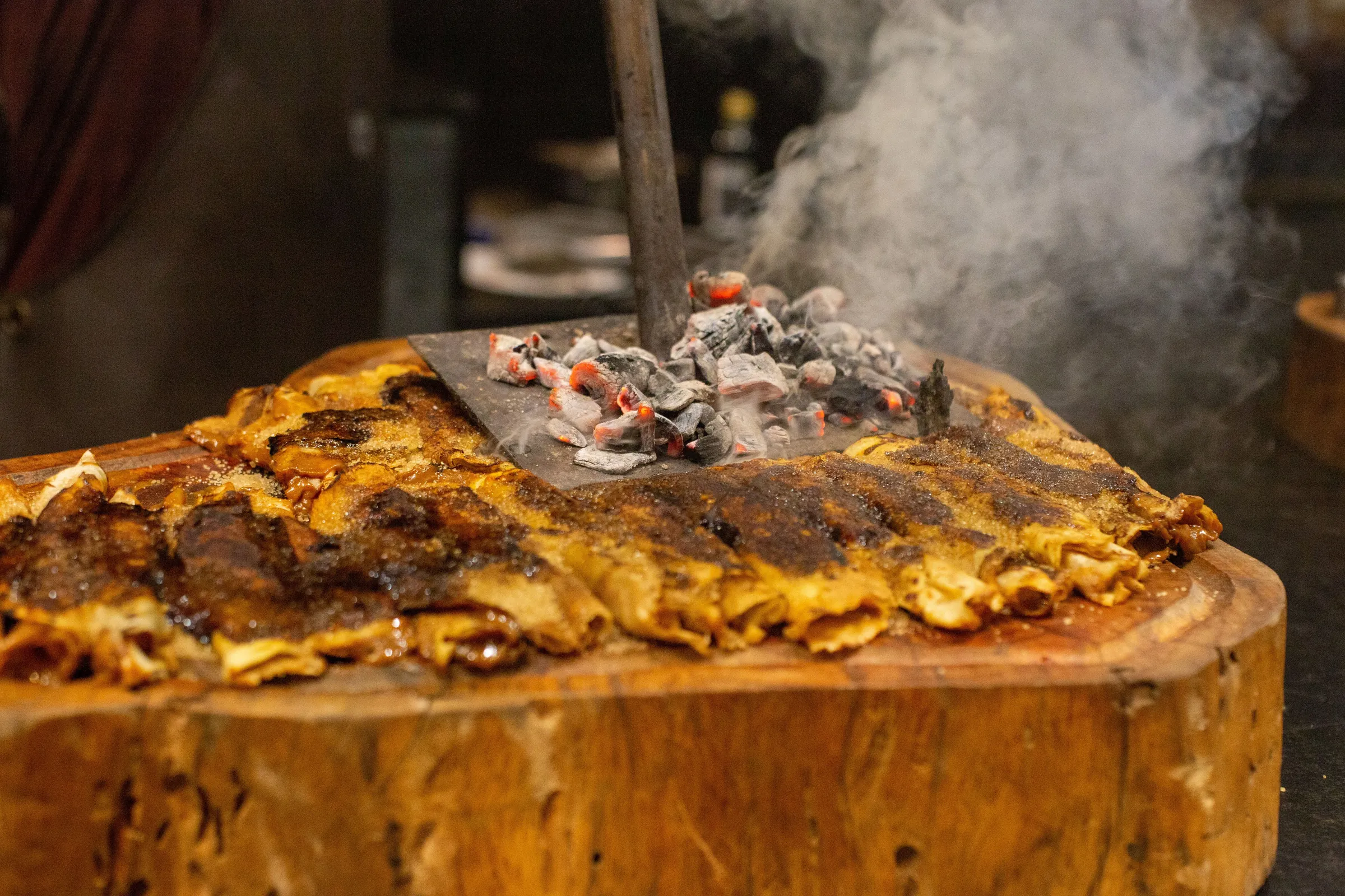 A steak resting on a wooden block with glowing embers piled on top