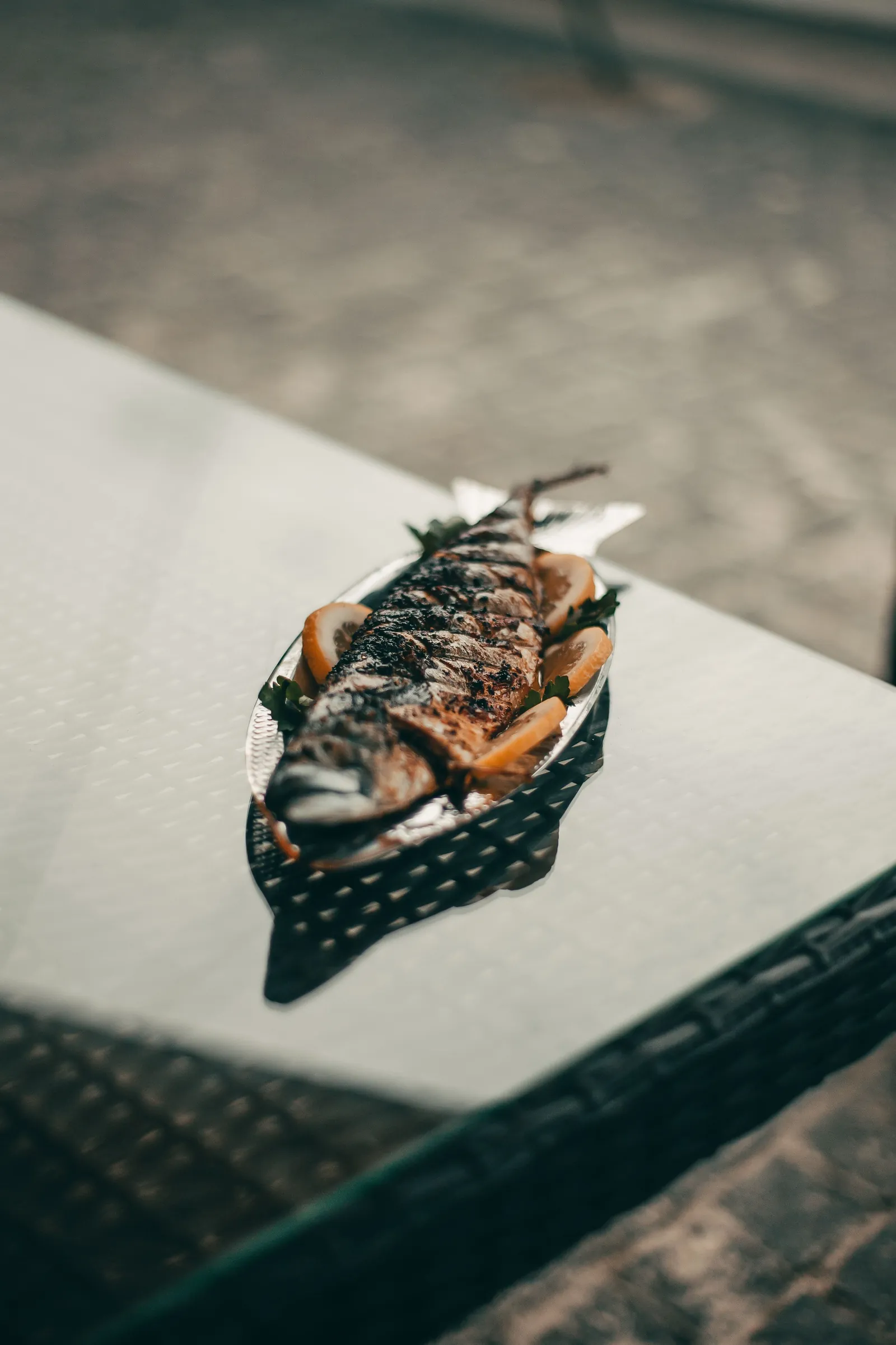 A whole grilled mackerel on a dark plate, the skin blistered and glossy