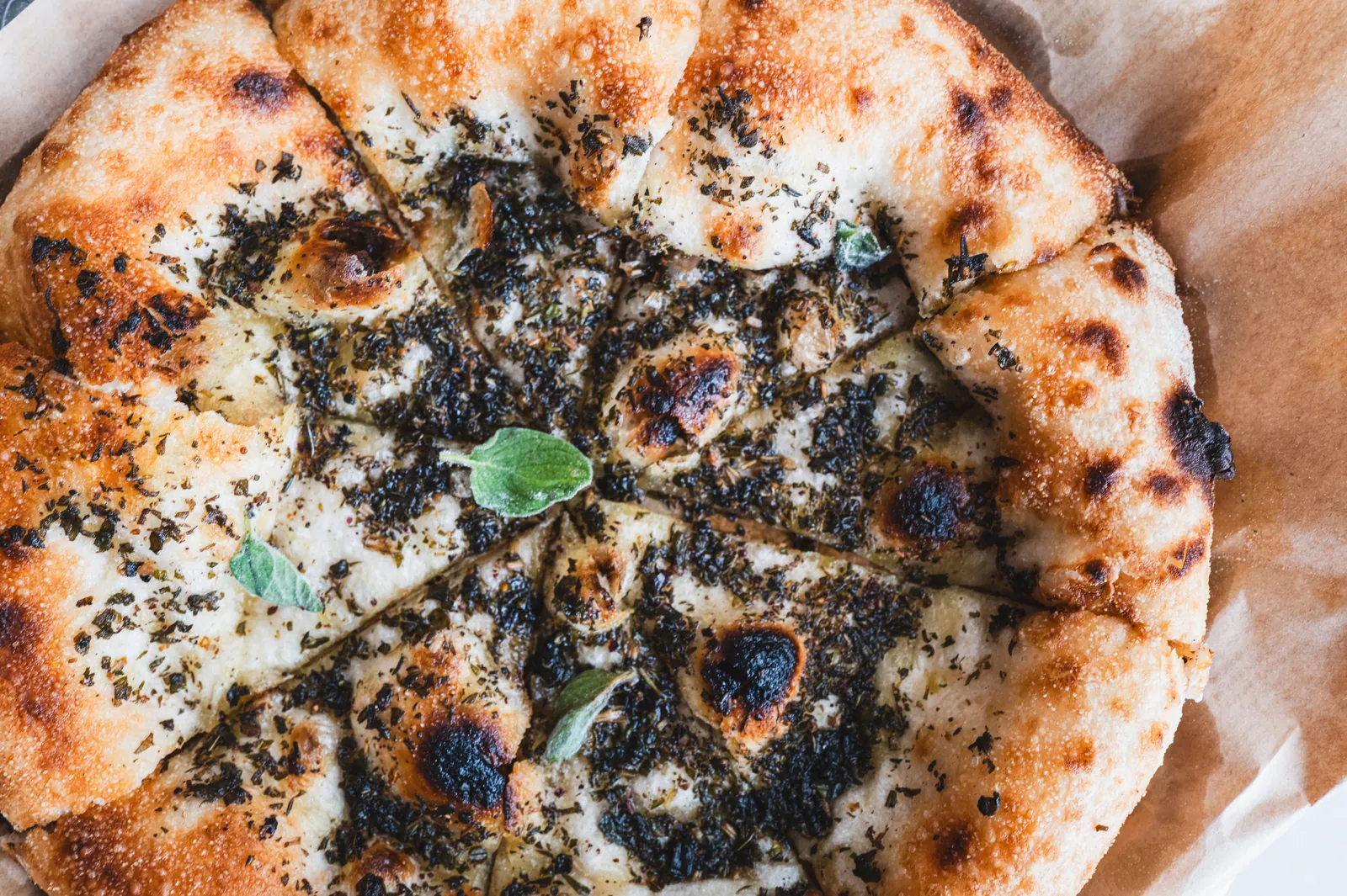 Blistered flatbread with charred edges and a herb topping, torn open