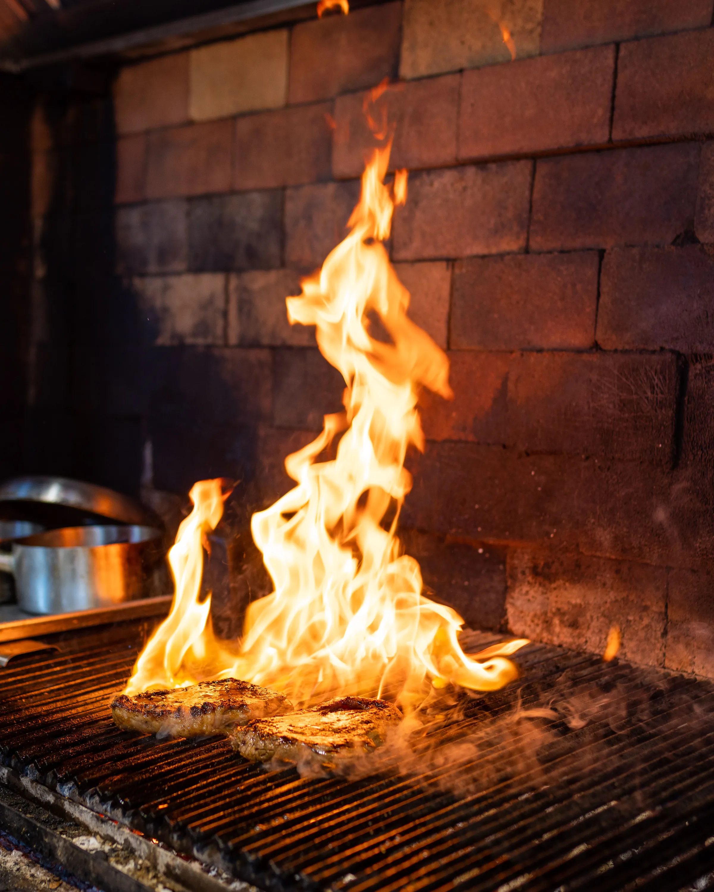 Flames leaping through the bars of a charcoal grill inside a brick hearth