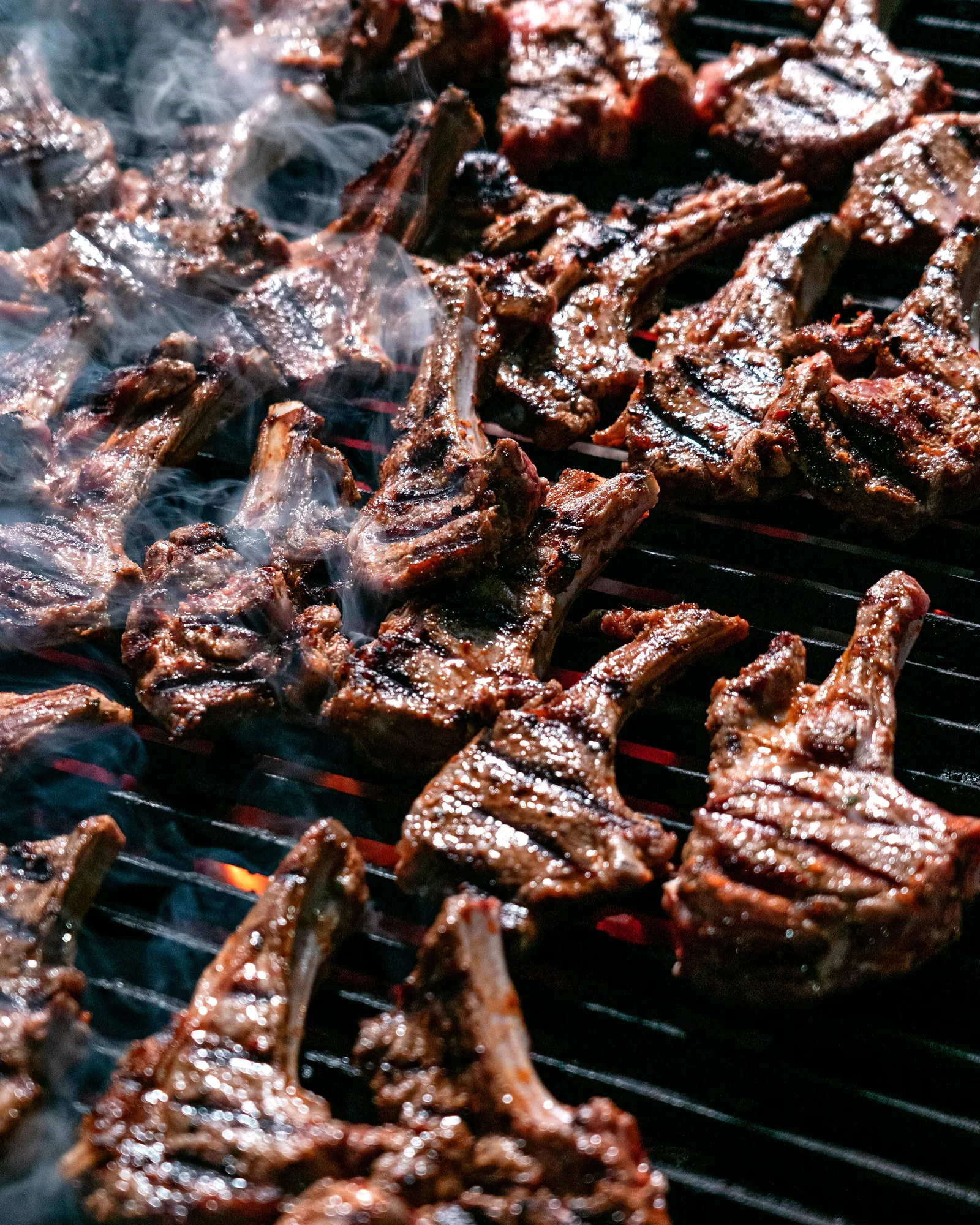 Lamb cutlets on the grill, edges caught by the flame, smoke rising