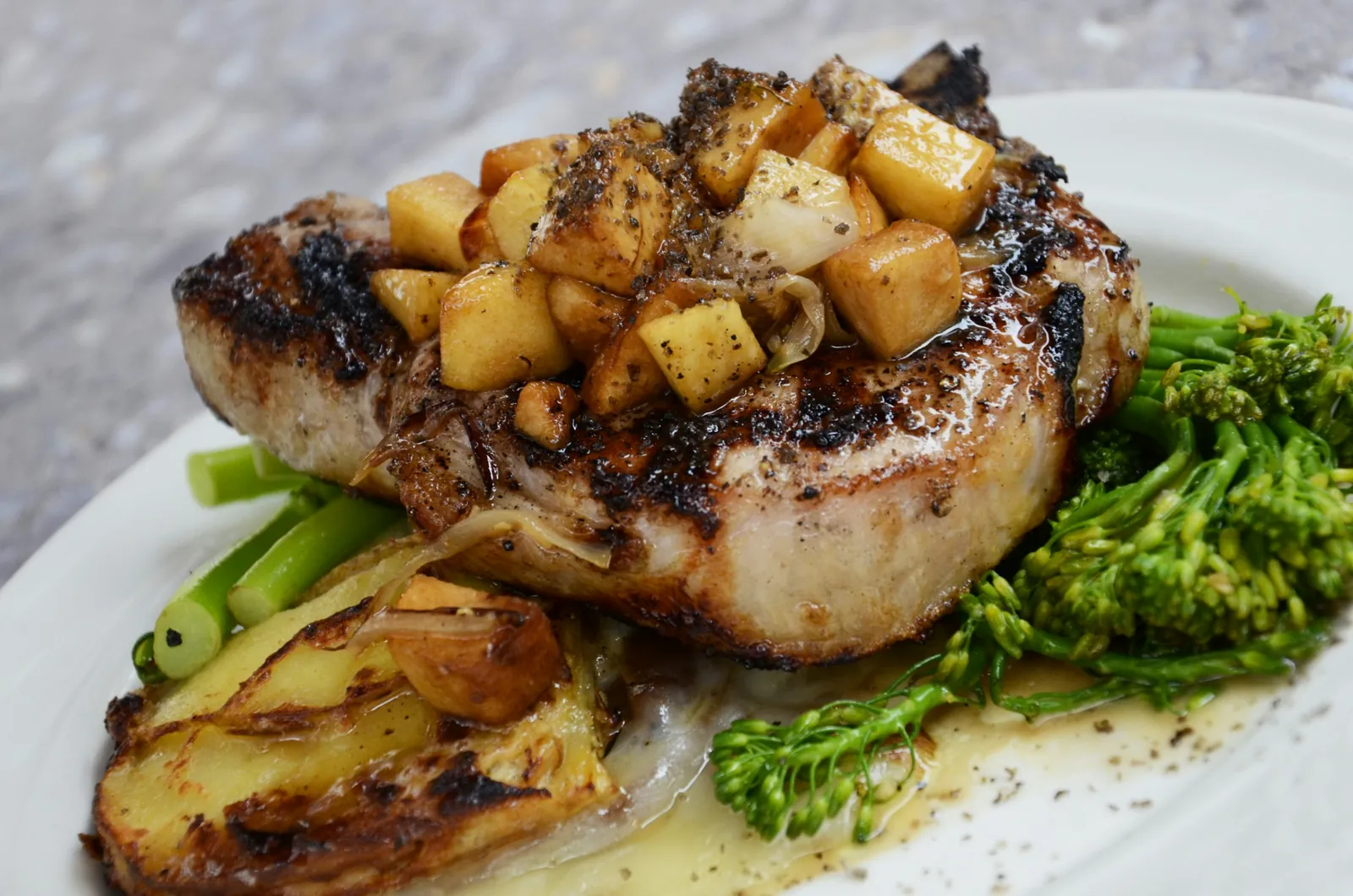 A grilled pork chop on the bone with charred potatoes and greens