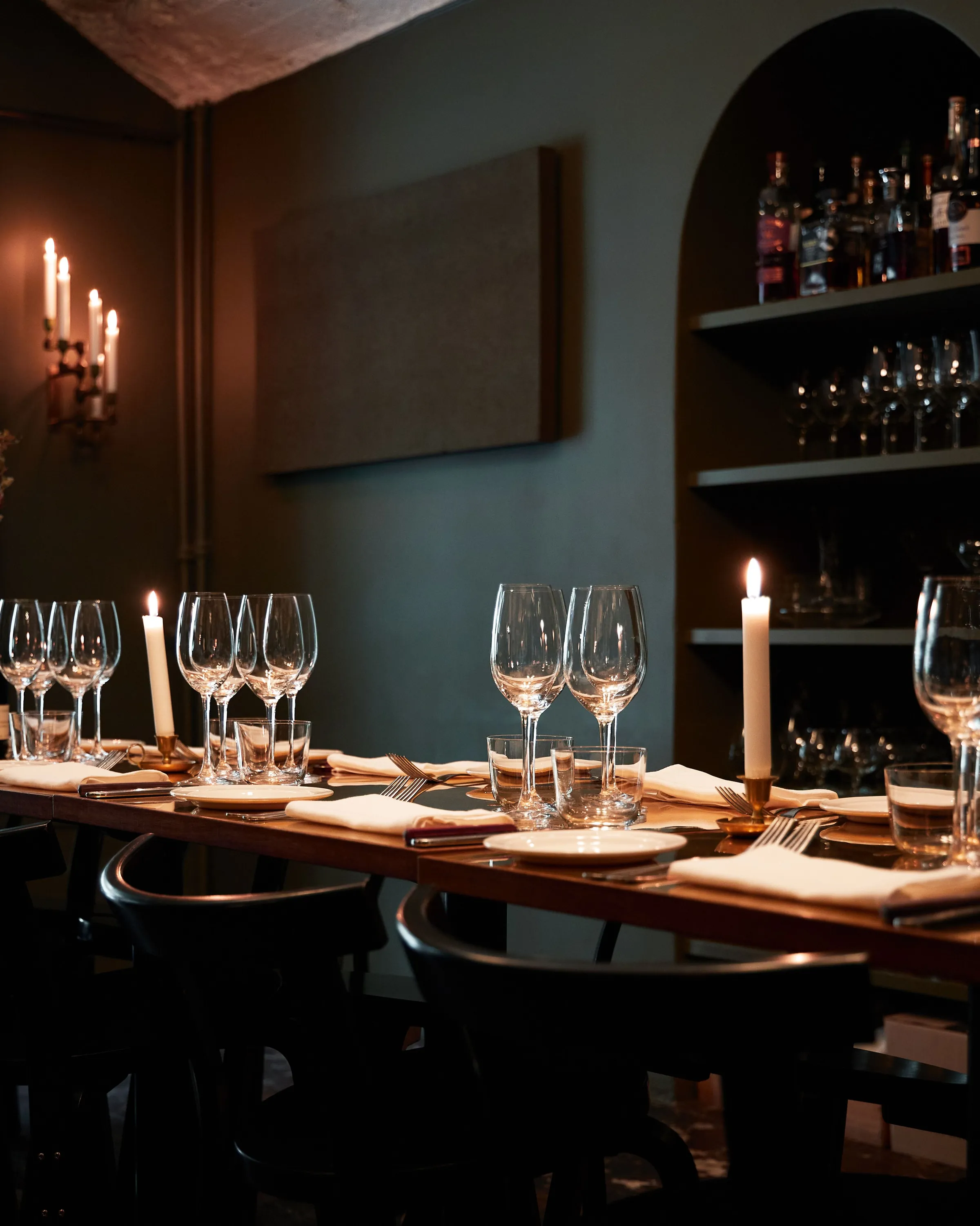 A private dining room with a candlelit table, glassware and shelves of bottles