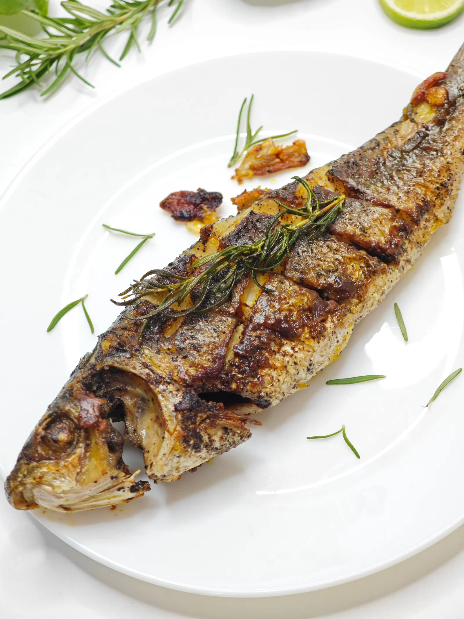A whole grilled sea bass on a white plate, skin blistered and charred