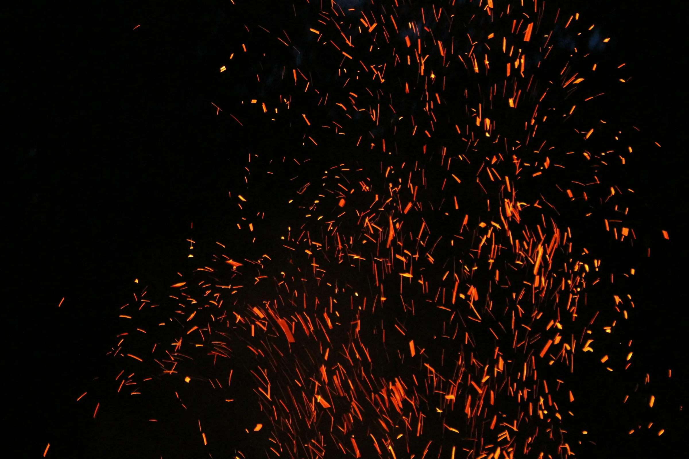Orange sparks rising from a fire against a black night sky