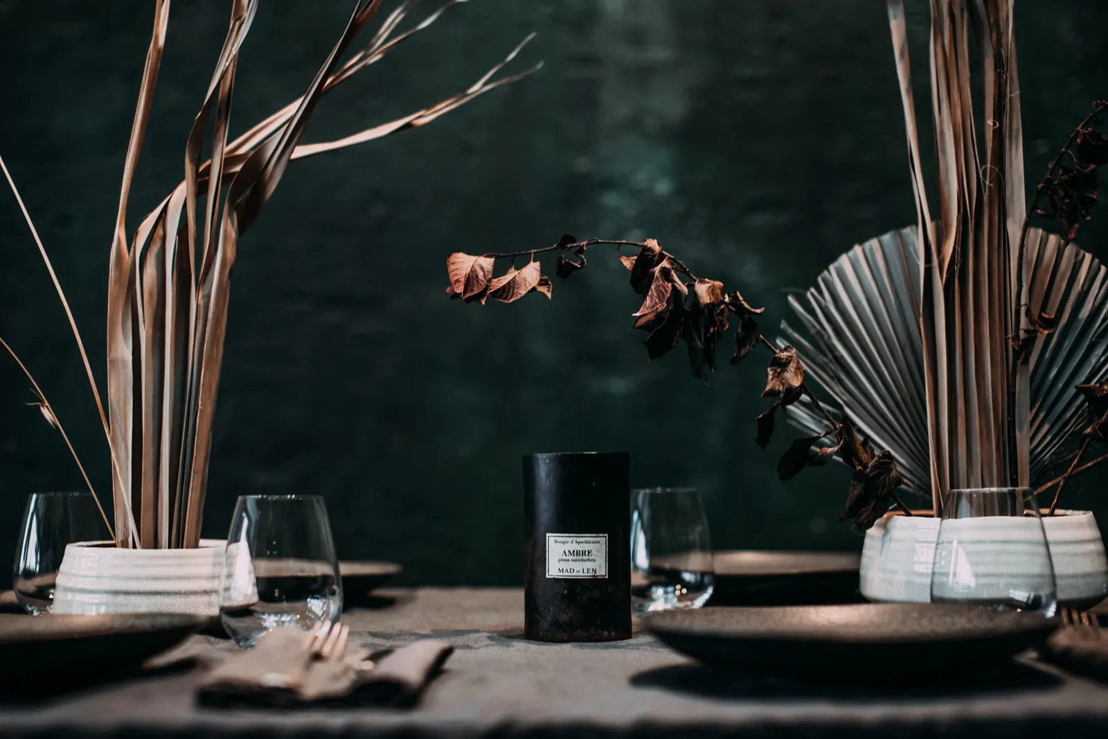 A dark-lacquered table laid with black plates, glasses and dried grasses