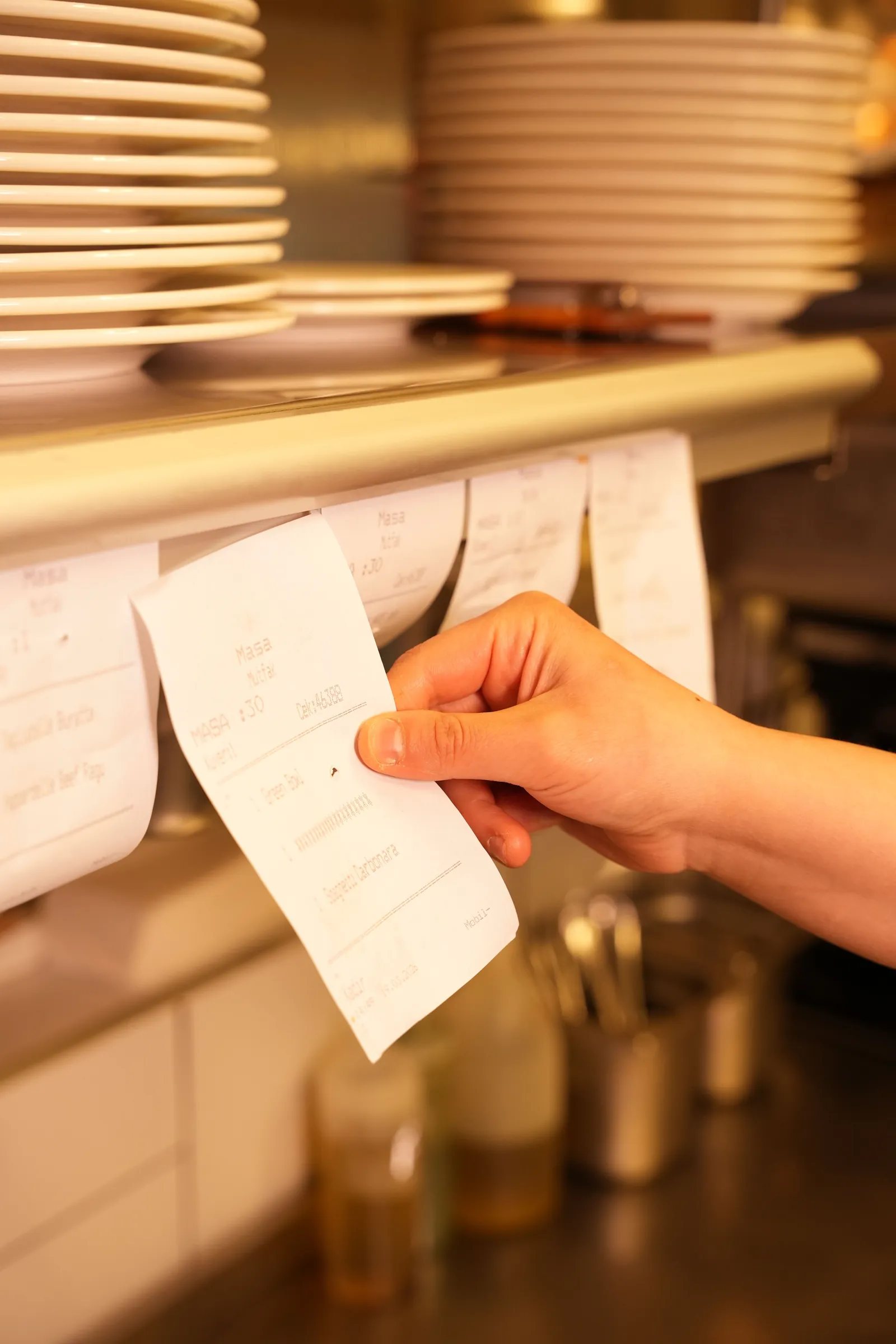 A hand pulling an order ticket from the rail above a kitchen pass