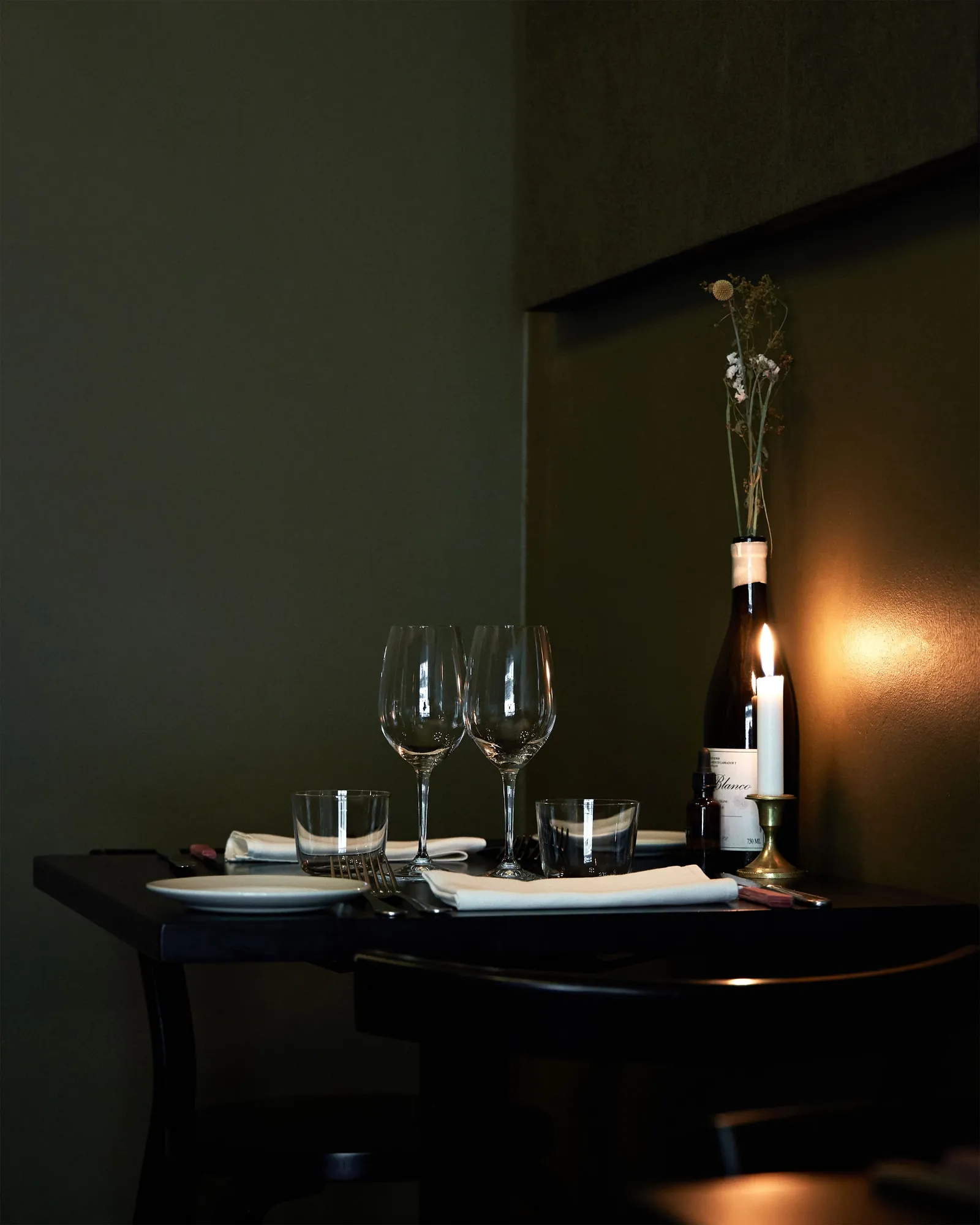 A single candle and an open bottle of wine on a dark table in a quiet room