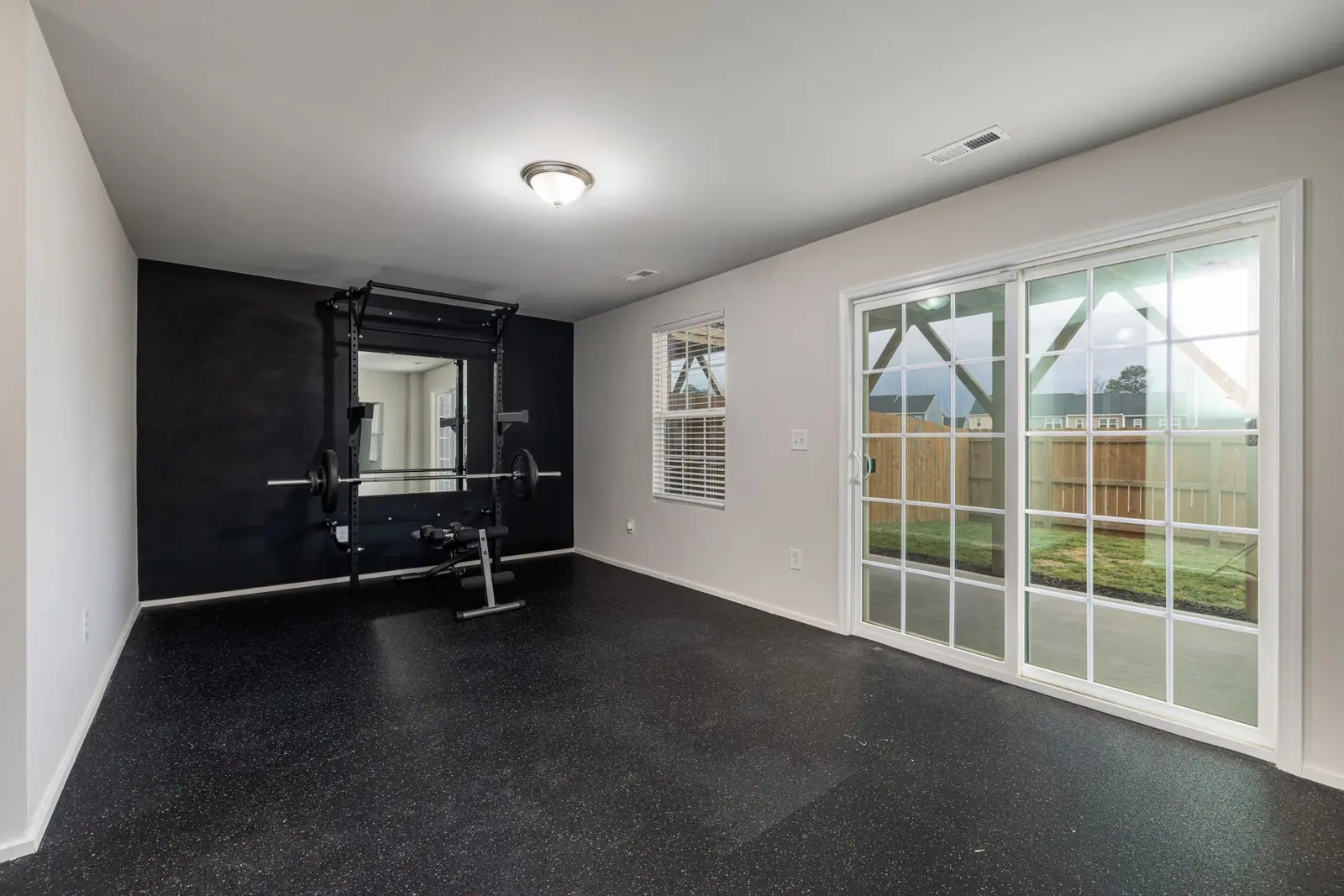 A home gym with a rubber floor, a squat rack against a dark wall and sliding doors onto a garden.