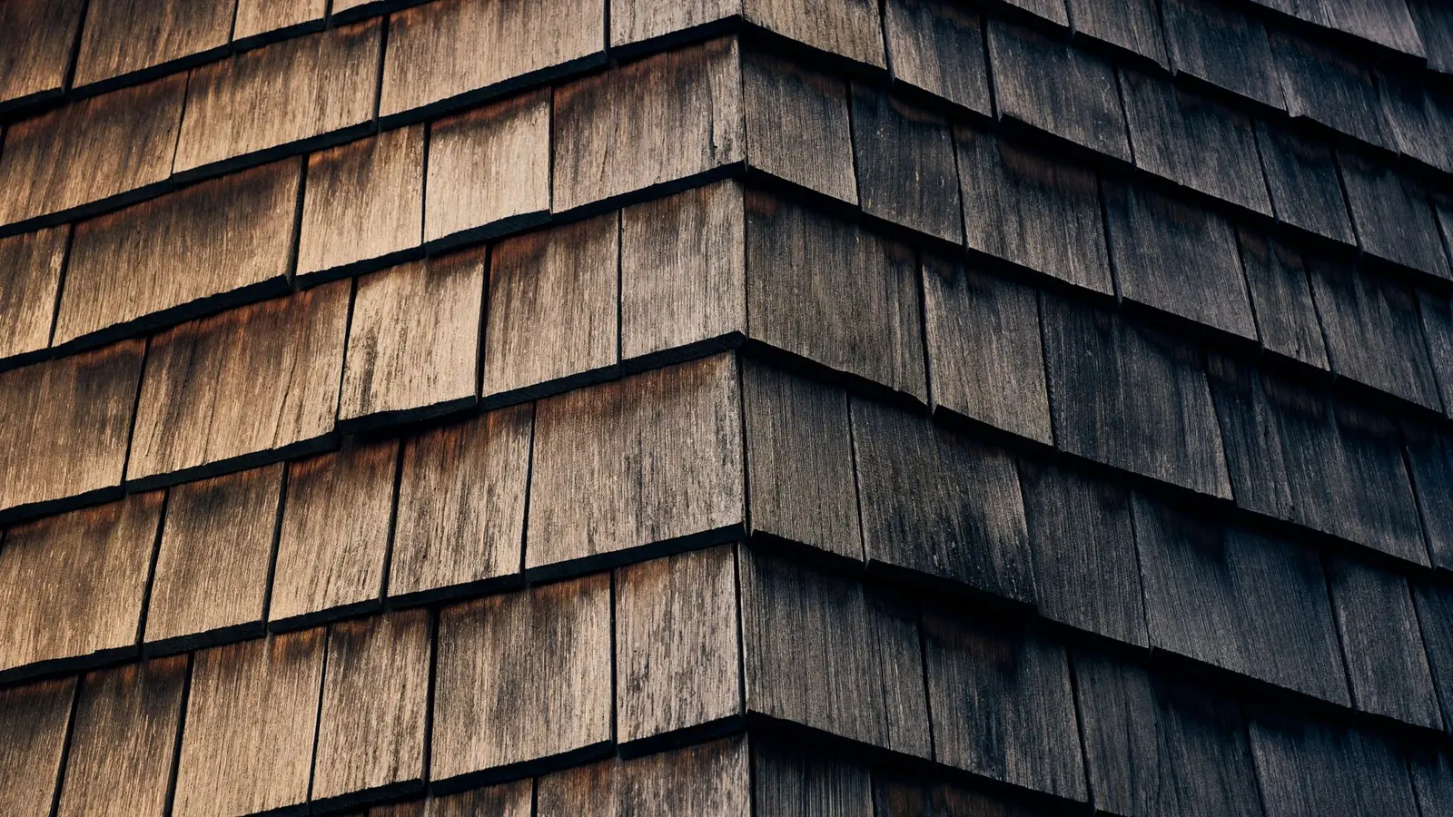 Weathered timber shingles on the corner of a building, close up, silvering along the exposed edges.