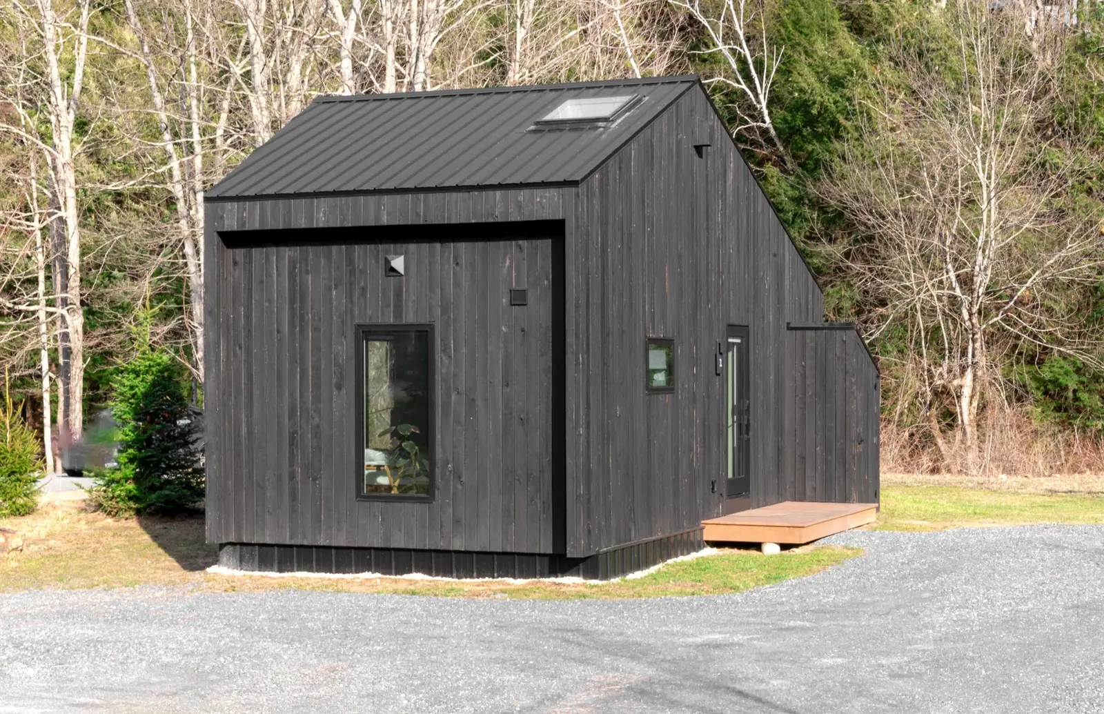 A black timber-clad garden building with a pitched roof, standing at the edge of a garden.