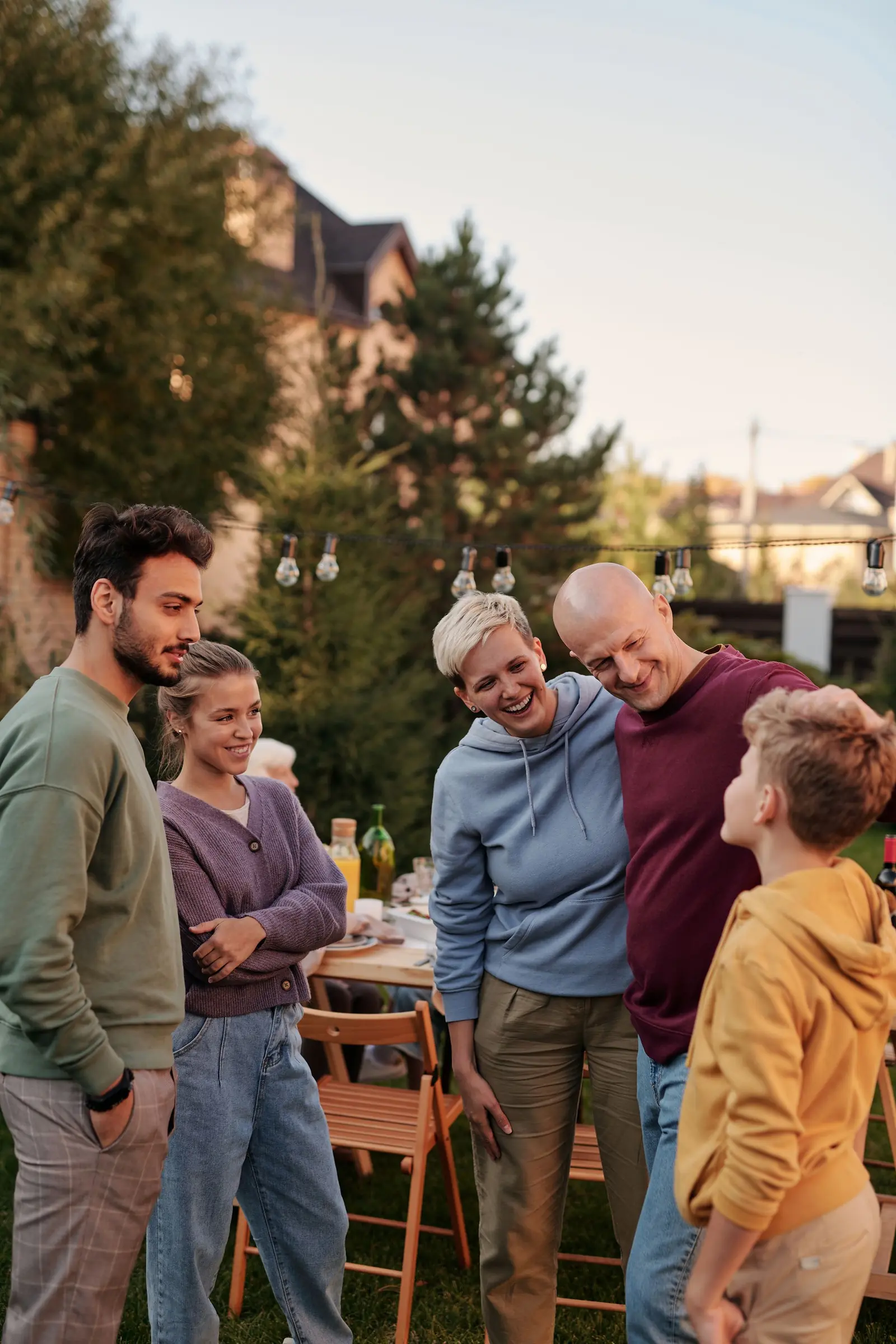 A family standing together in a garden on a summer evening, houses and trees behind them.