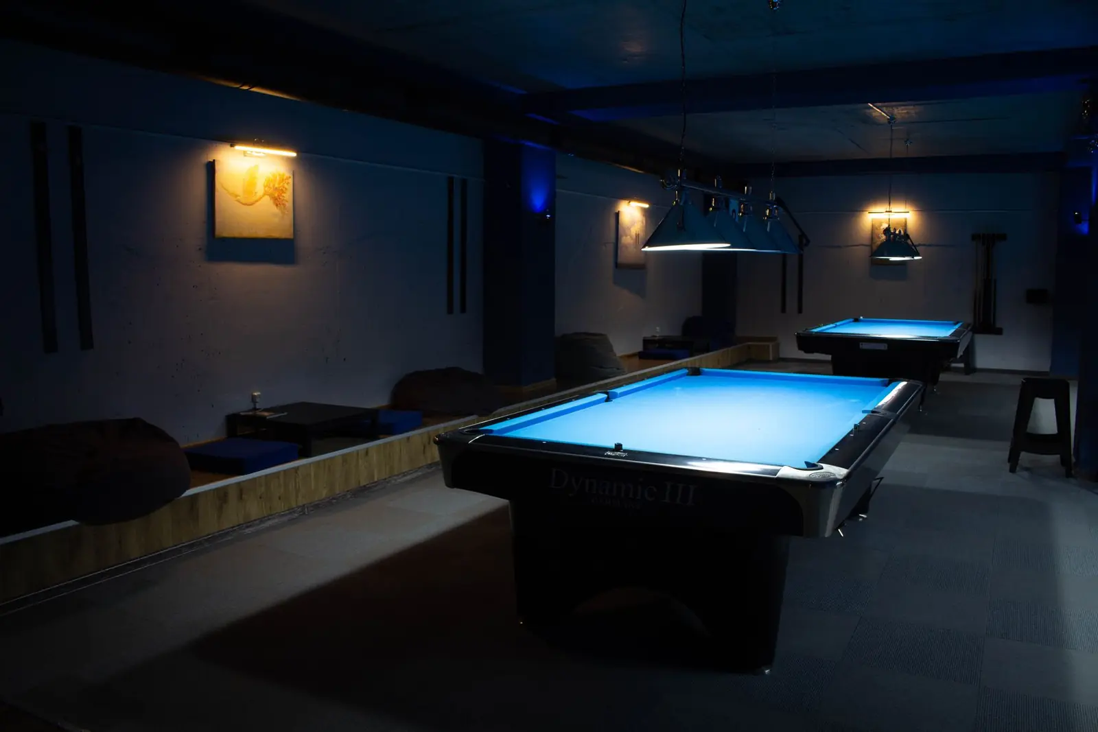 A darkened games room with a pool table lit from above and low seating around the edge.