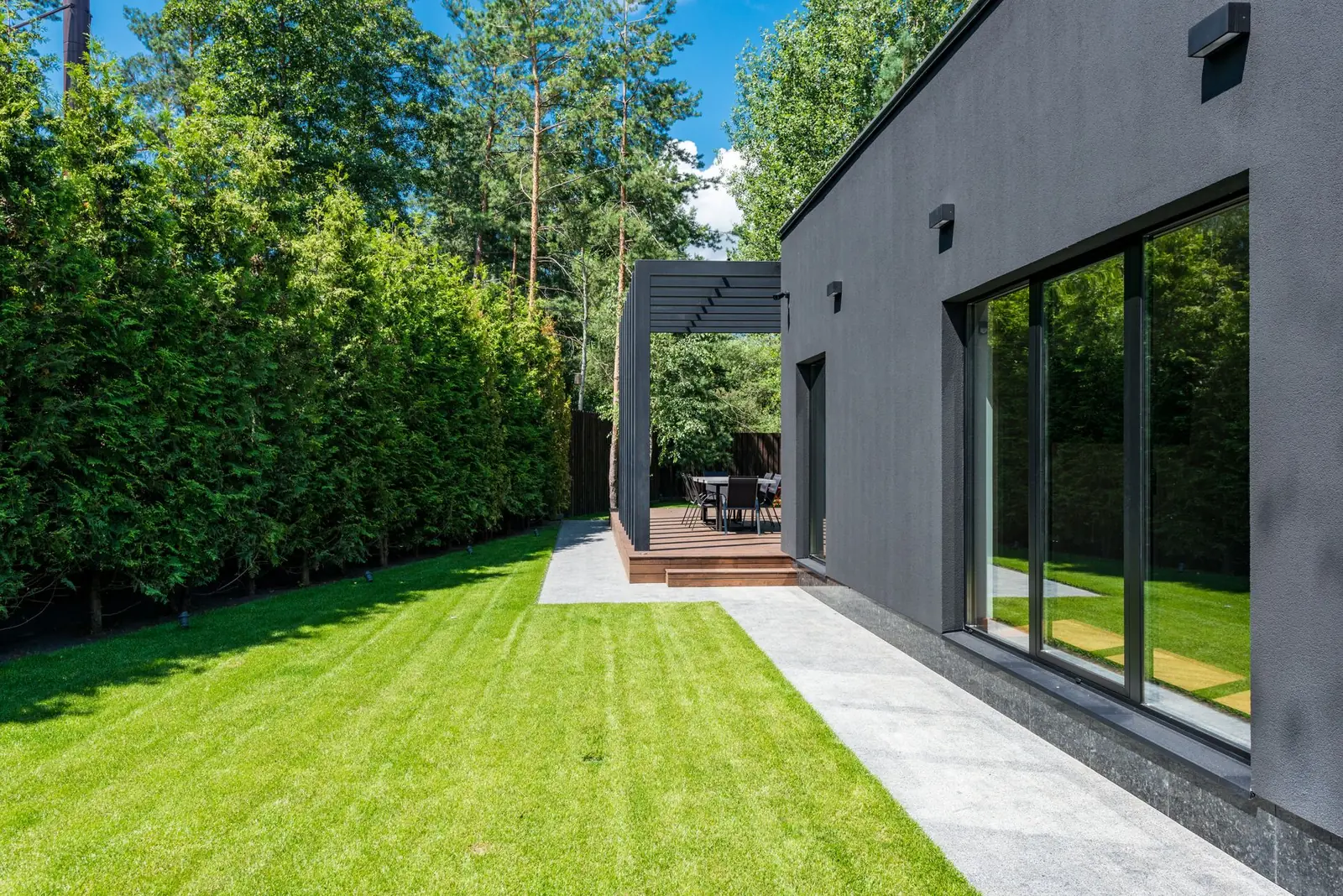 A garden building with full-height sliding glass doors at the end of a striped lawn, hedges either side.